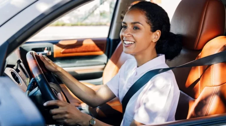 smiling lady in the driver's seat of a car wearing a seatbelt and holding the steering wheel